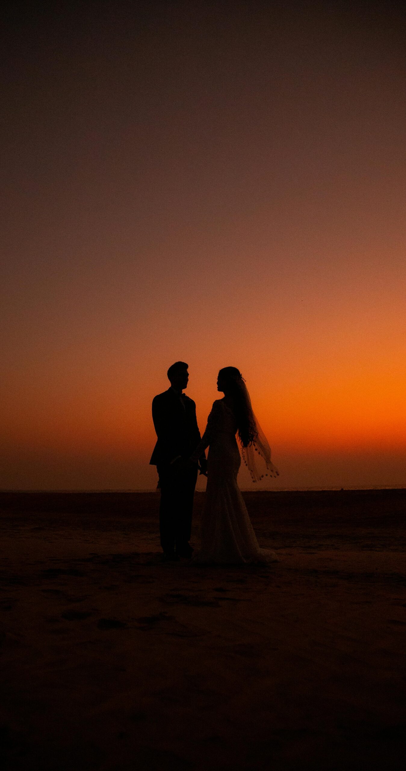 Silhouette of a couple holding hands on a beach at sunset, capturing love and romance.