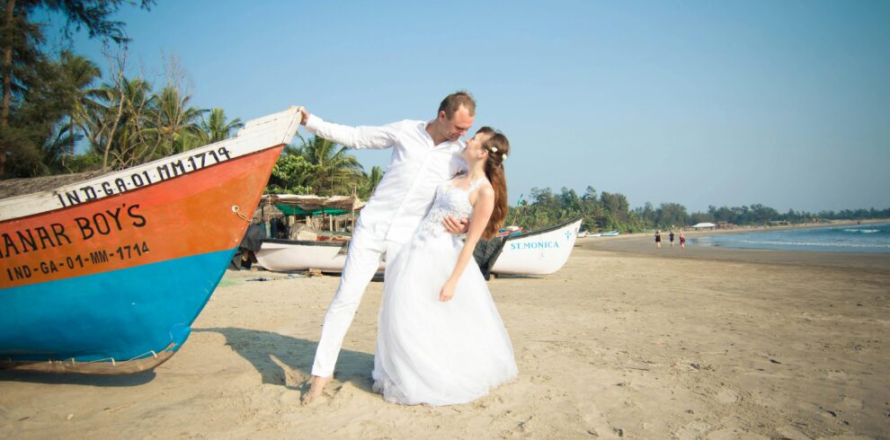 Bride and groom share a romantic moment on a tropical beach with colorful boats in the background.