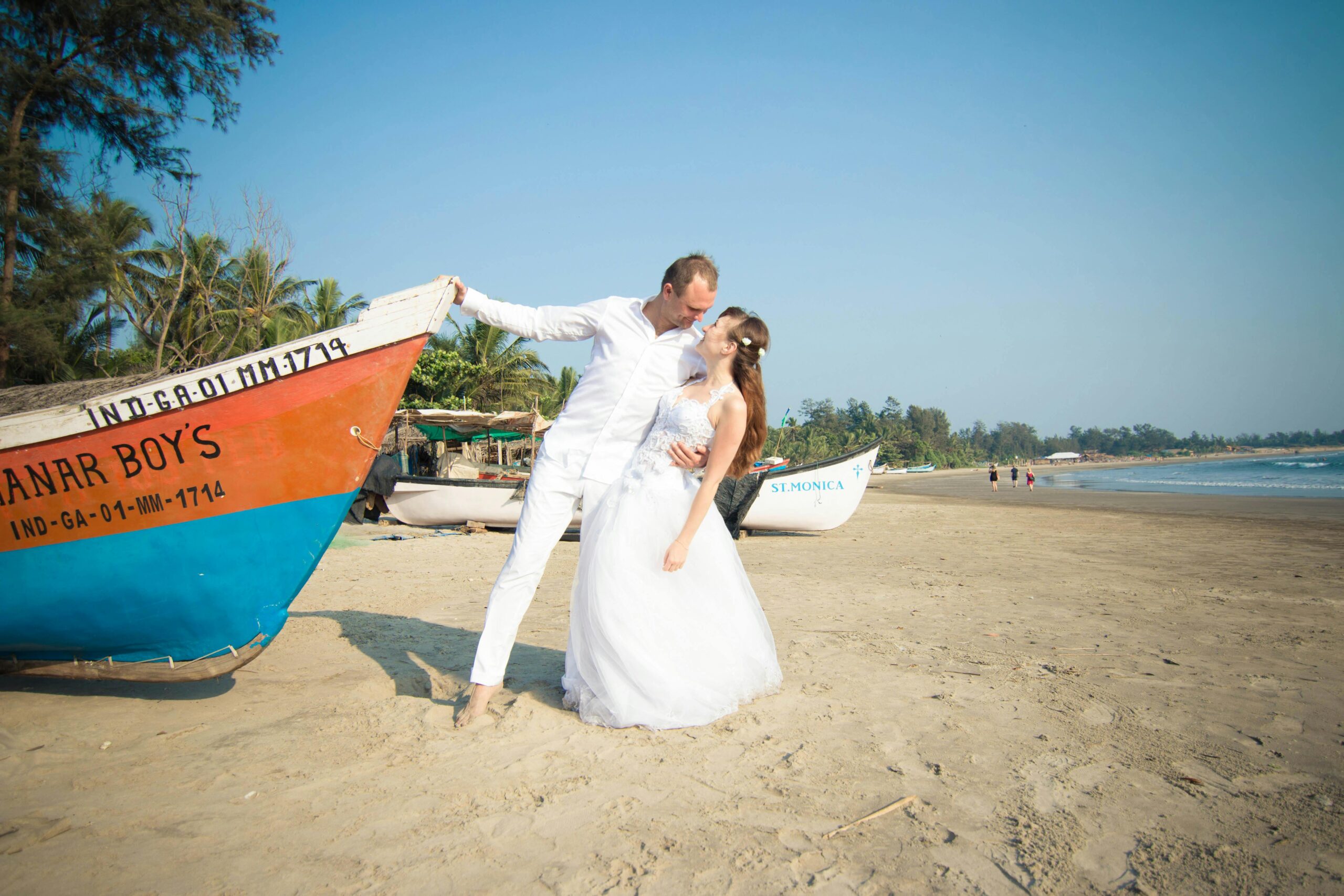 Bride and groom share a romantic moment on a tropical beach with colorful boats in the background.